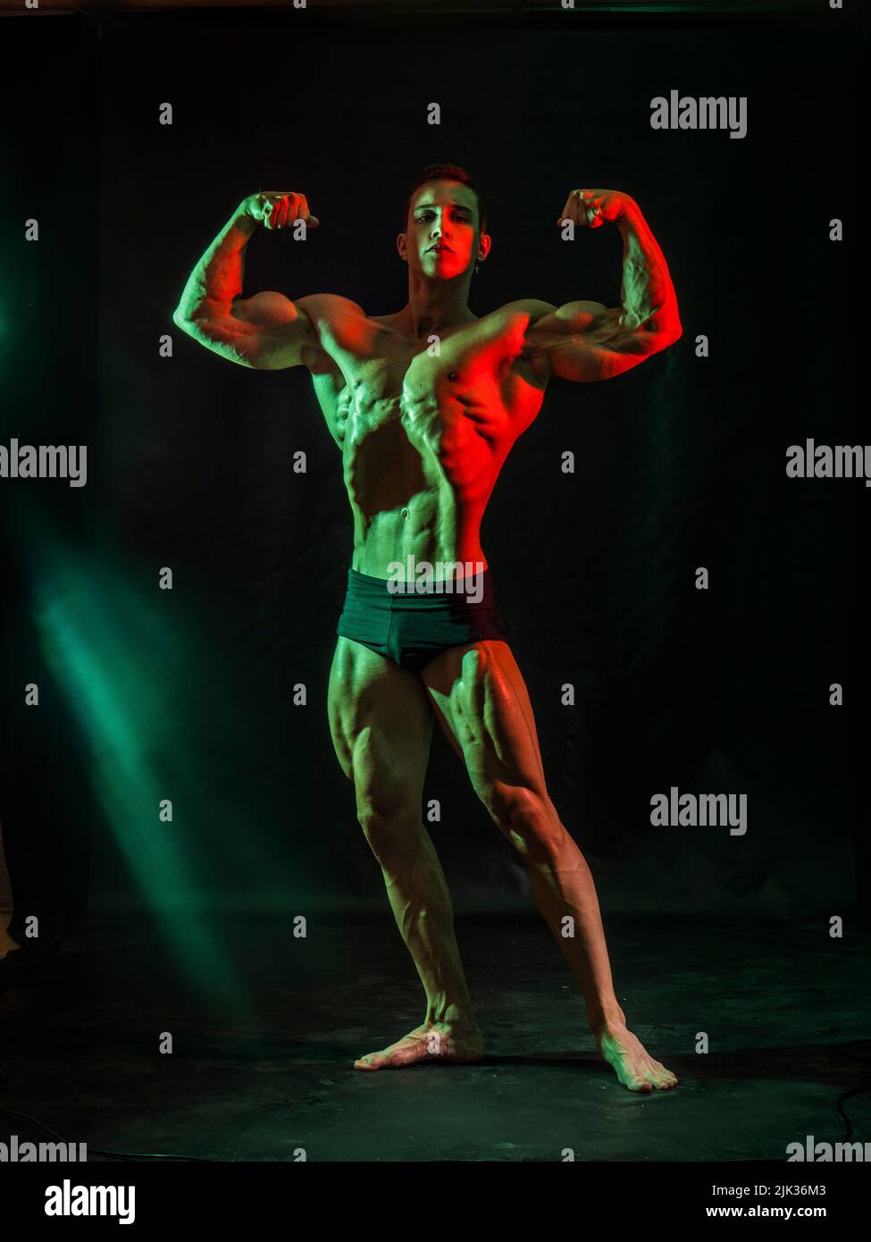 Handsome bodybuilder doing classic double biceps pose, looking away, on dark background Stock Photo