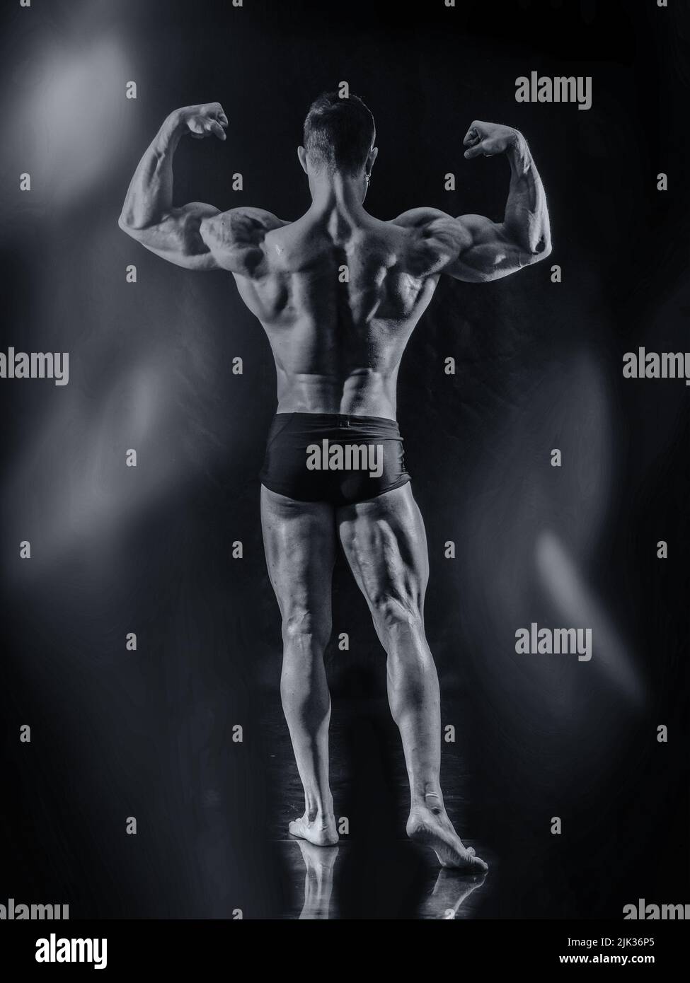 Handsome bodybuilder doing classic back double biceps pose, looking away, on dark background Stock Photo