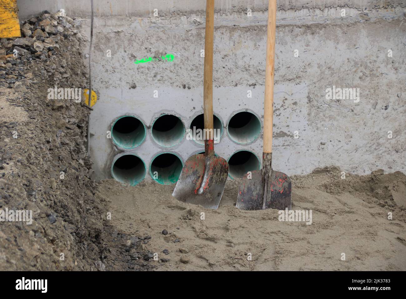 2 shovels stand on a wall with openings for cables Stock Photo