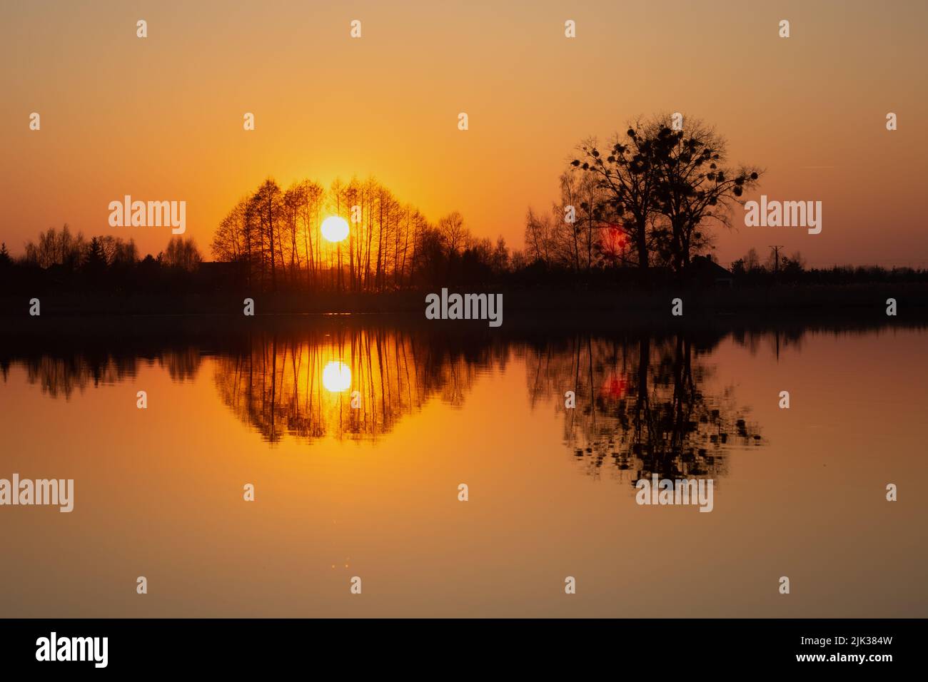 The reflection in the water of the sunset behind the trees, spring evening view Stock Photo