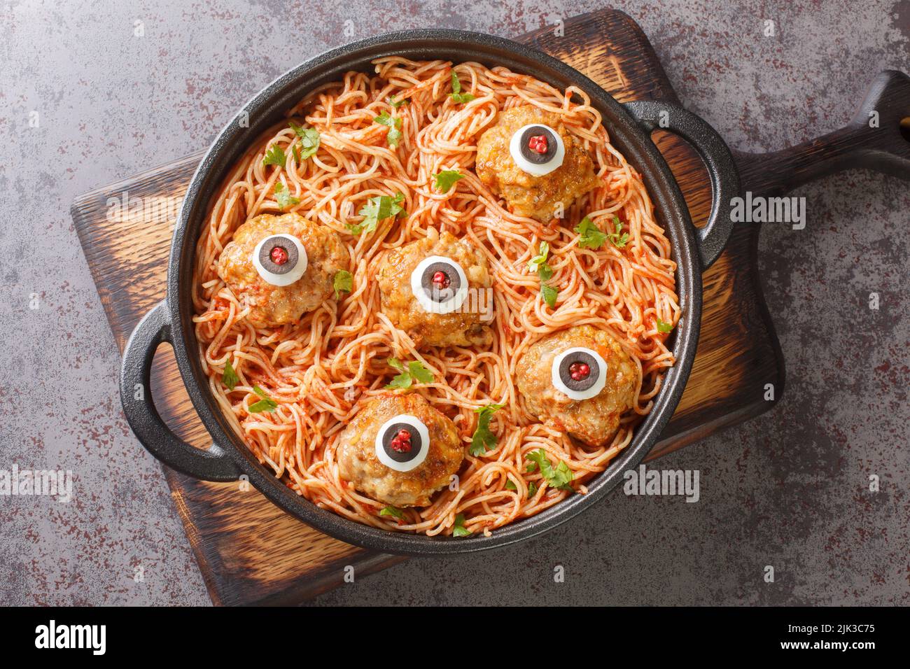 Scary Halloween food of meatballs with monster eyes and pasta with tomato sauce in a frying pan on the table close-up. Horizontal top view from above Stock Photo