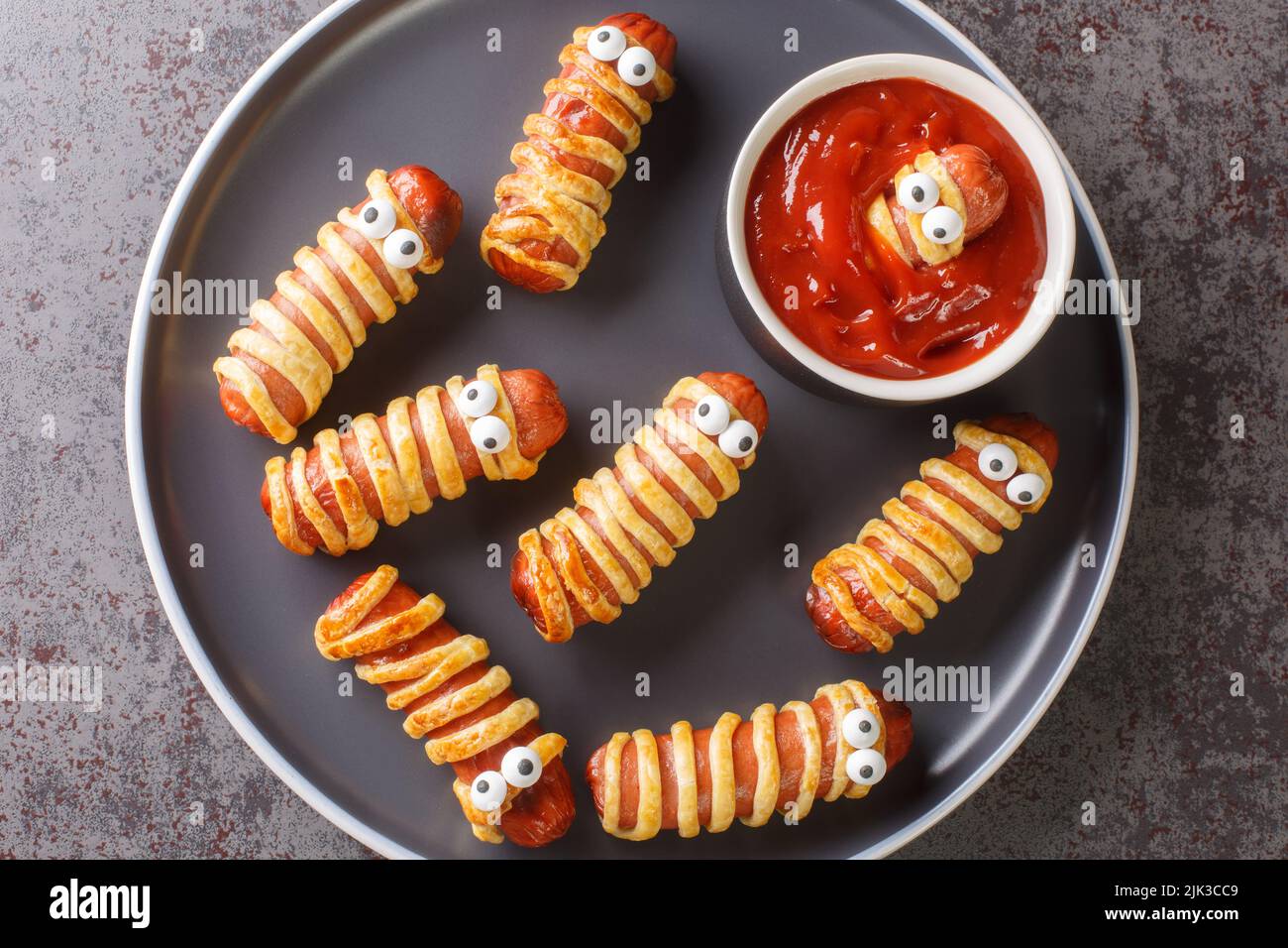 sausage baked in pastry mummy food for Halloween party or children's holiday closeup in the plate on the table. Horizontal top view from above Stock Photo