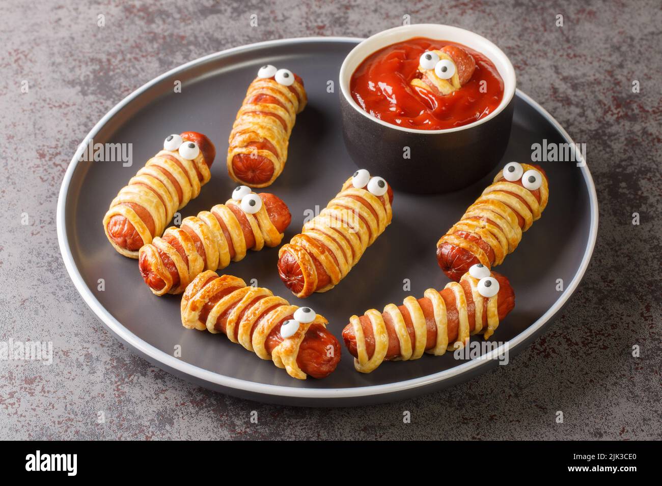 Funny sausage mummies in dough with ketchup for the Halloween party. Children's food closeup in the plate on the table. Horizontal Stock Photo