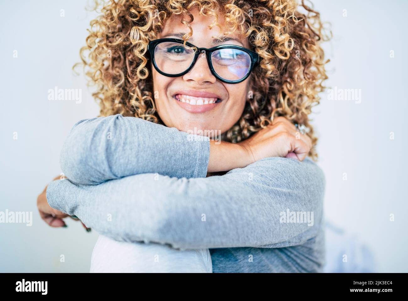 Portrait of young adult woman smiling at the camera and wear glasses. Blonde curly long hair female enjoy life. Happy and cheerful lady smile. Front v Stock Photo