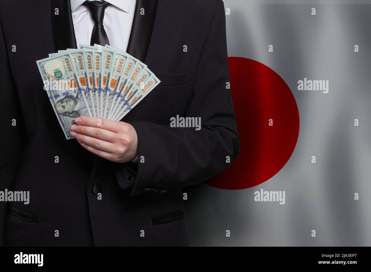 Japanese business man showing 100 US dollar bills against flag of Japan