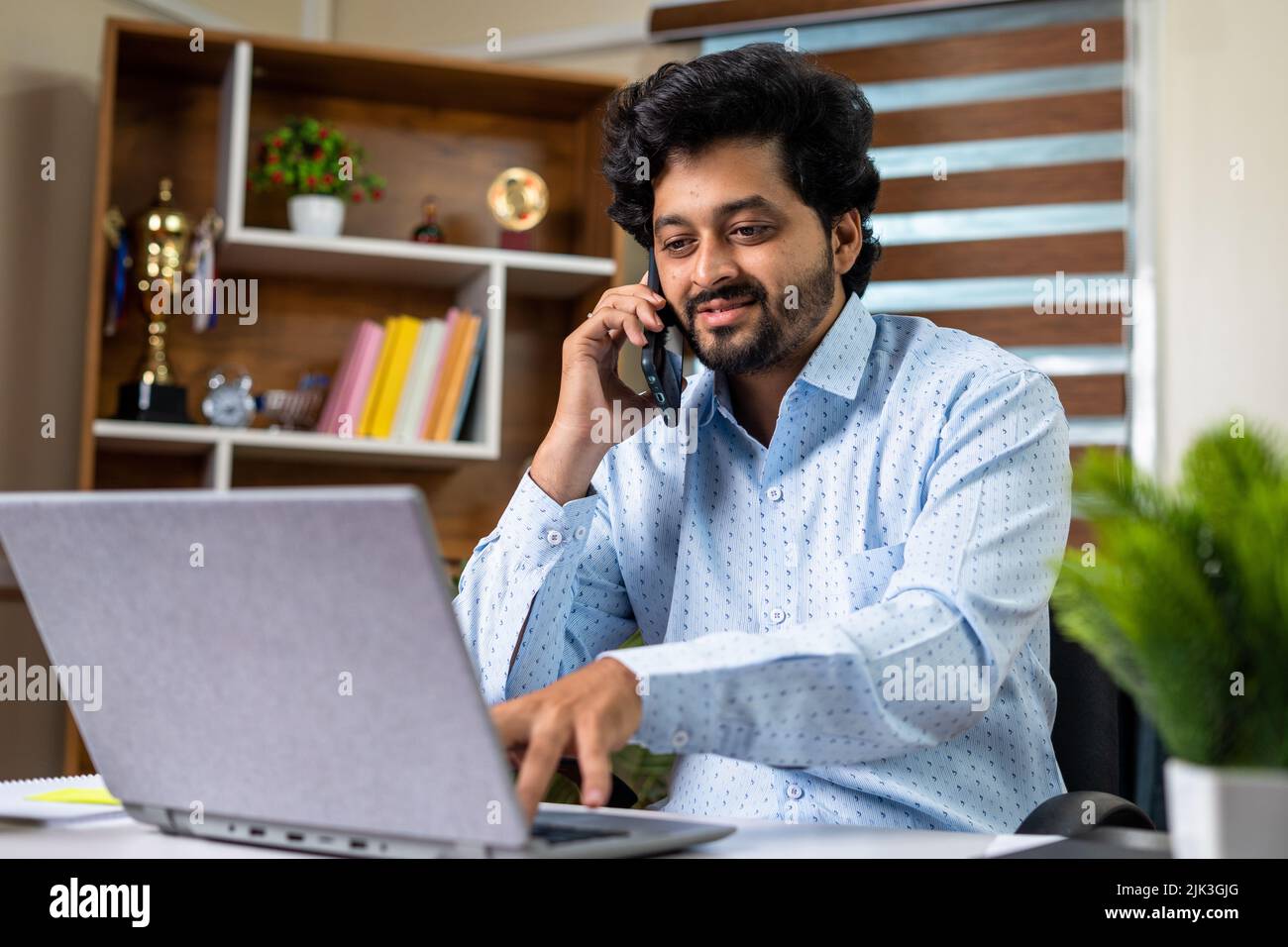 Happy businessman talking with client on mobile phone while working laptop at office - concept of consultation, financial advisor and white collar Stock Photo