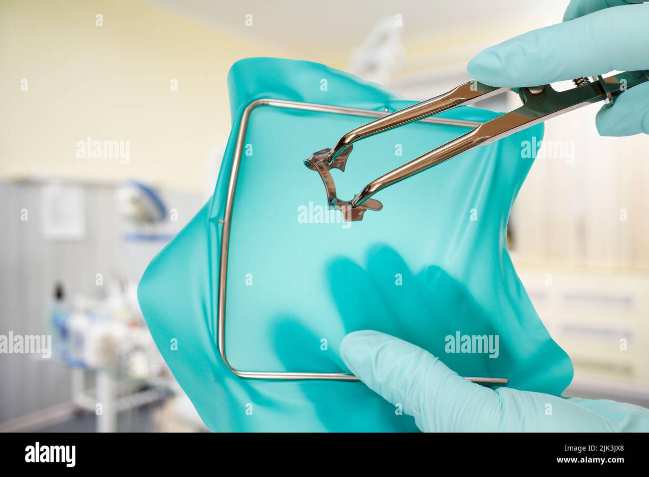 Dentist's hands in gloves with a rubber dam clamp forceps and cofferdam