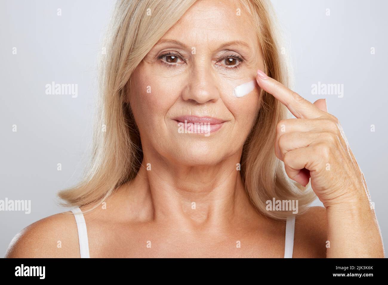 An attractive blond senior woman putting anti-age creme. Beauty photography Stock Photo