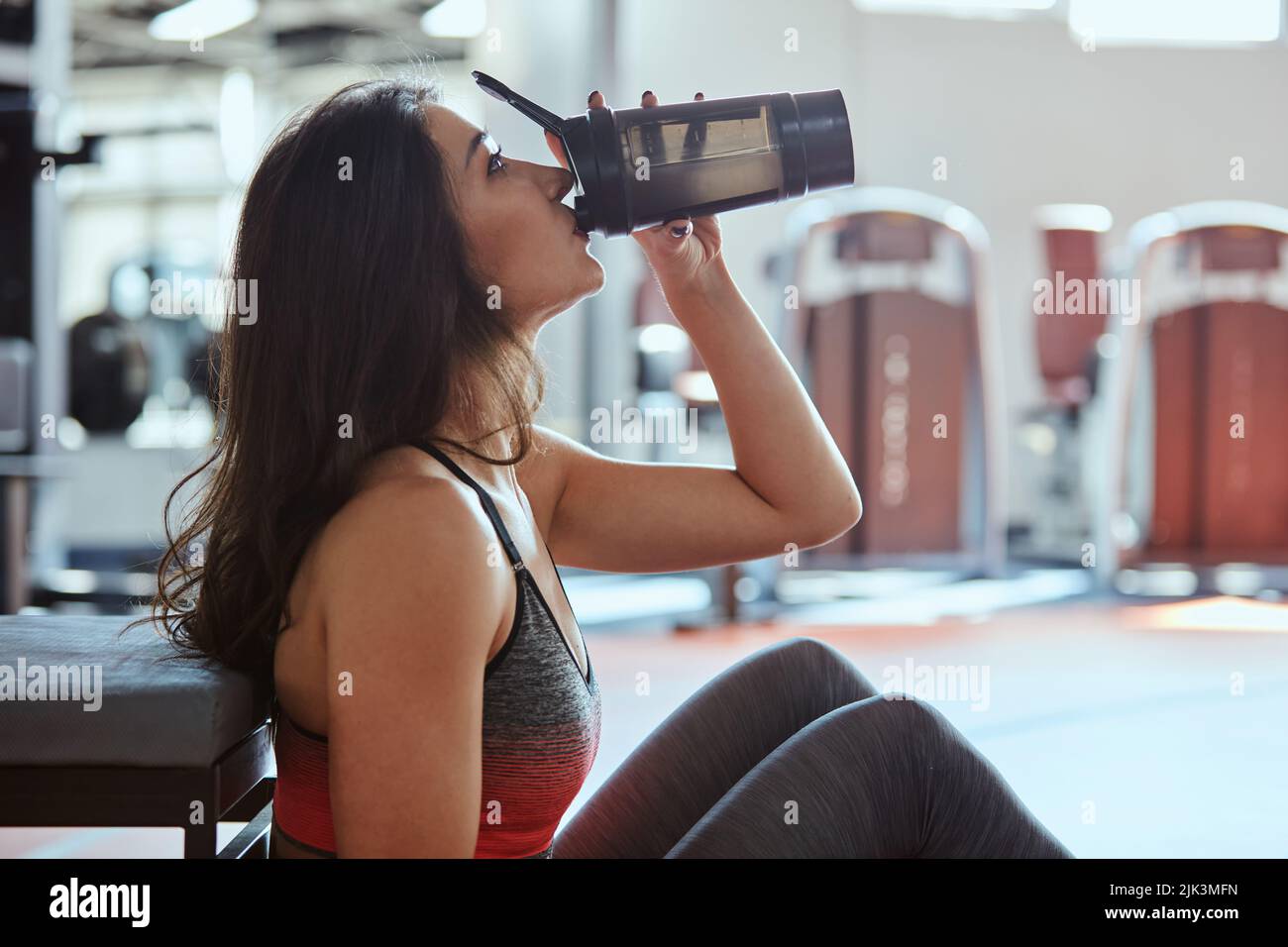 Young active woman taking a break in the gym and drinking protein shake. Stock Photo