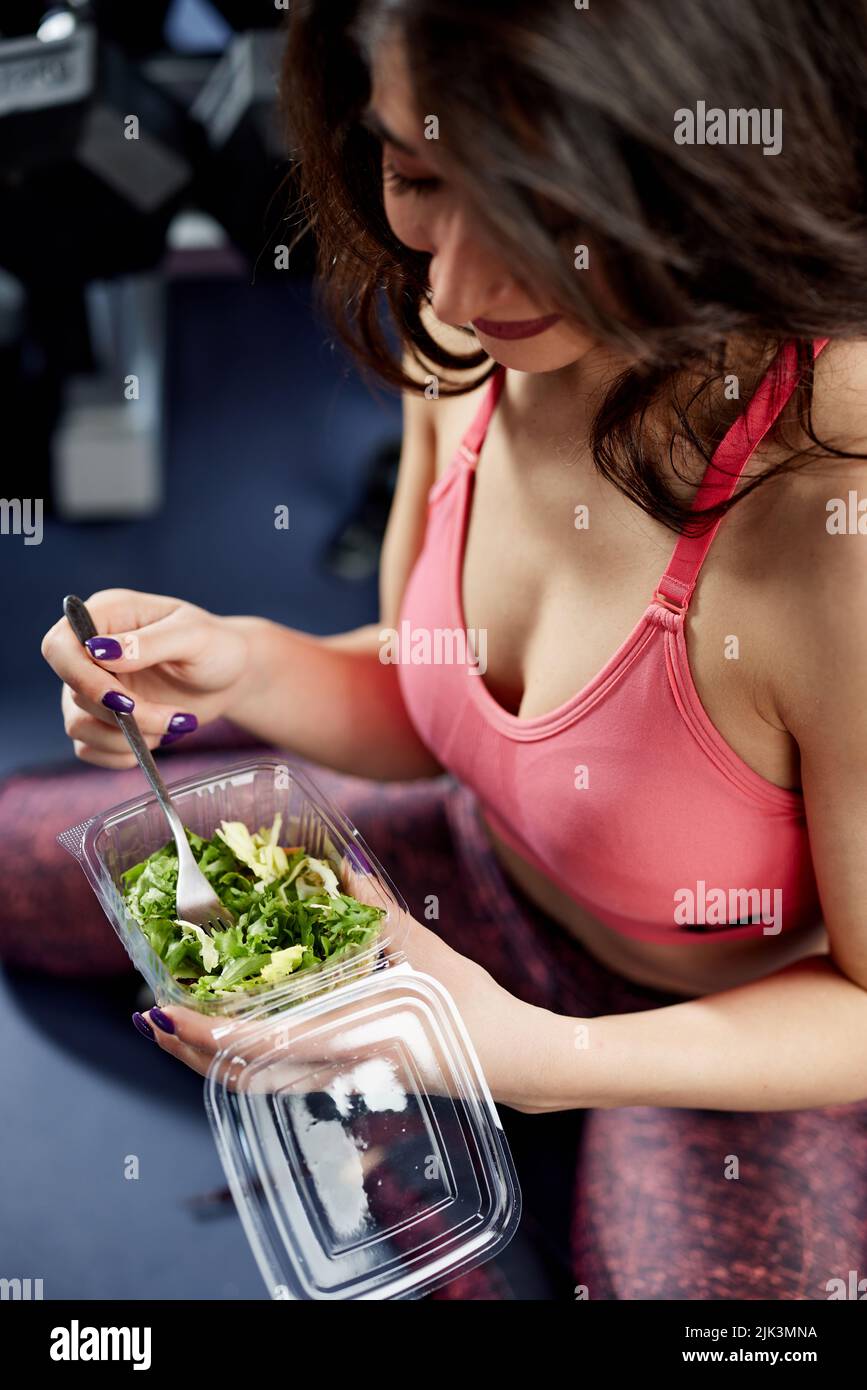 Attractive sportswoman in workout clothes eating a healthy salad in a gym. Stock Photo