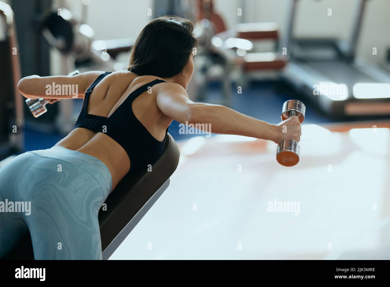 A strong, muscular female weightlifter is doing exercises on a bench with dumbbells for backs