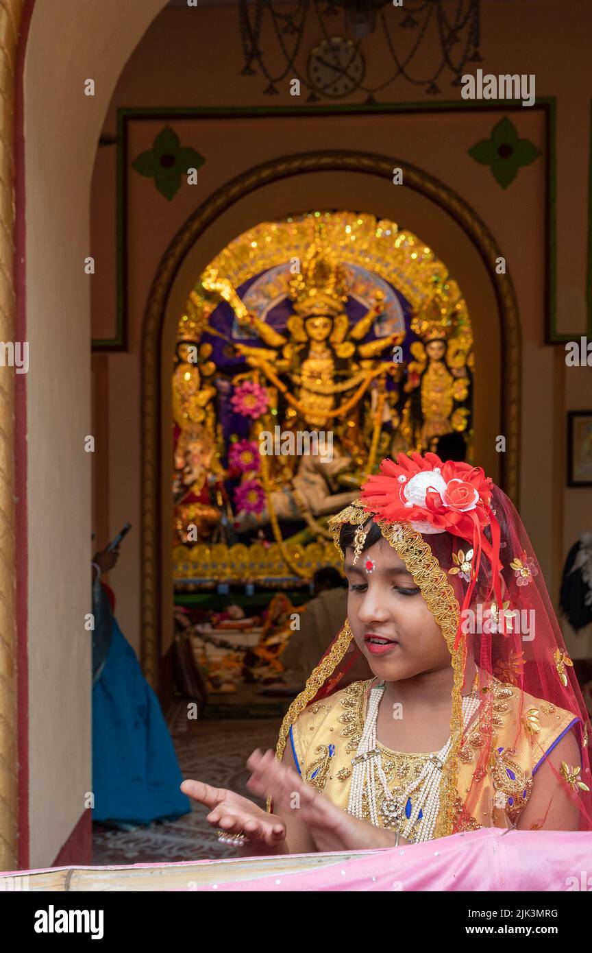 Howrah,India -October 26th,2020 : Bengali girl child in festive dress, smiling and posing with Goddess Durga in background, inside old age decorated h Stock Photo