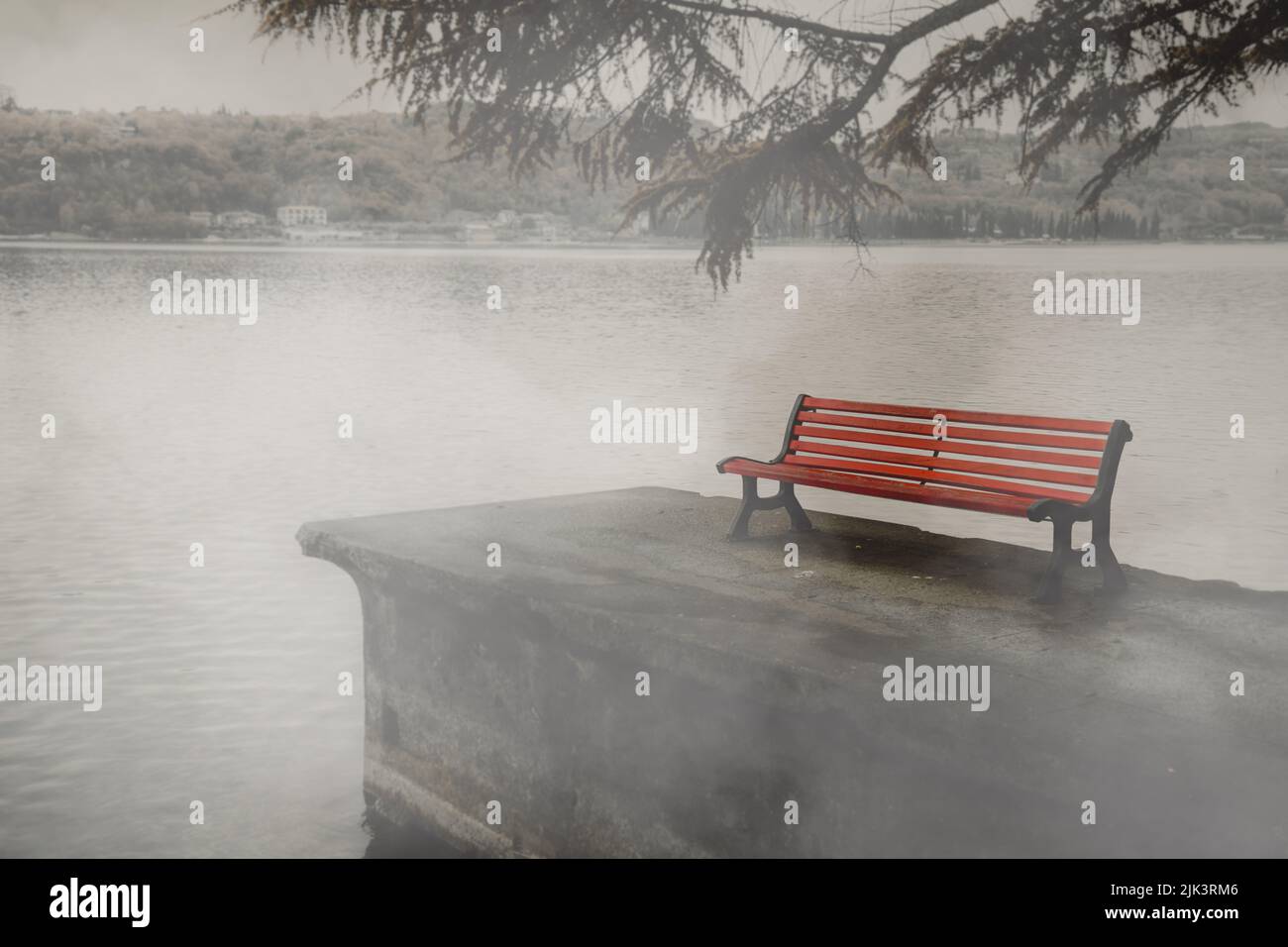 A red park bench at the lake in the fog, concept of grief and loss Stock Photo