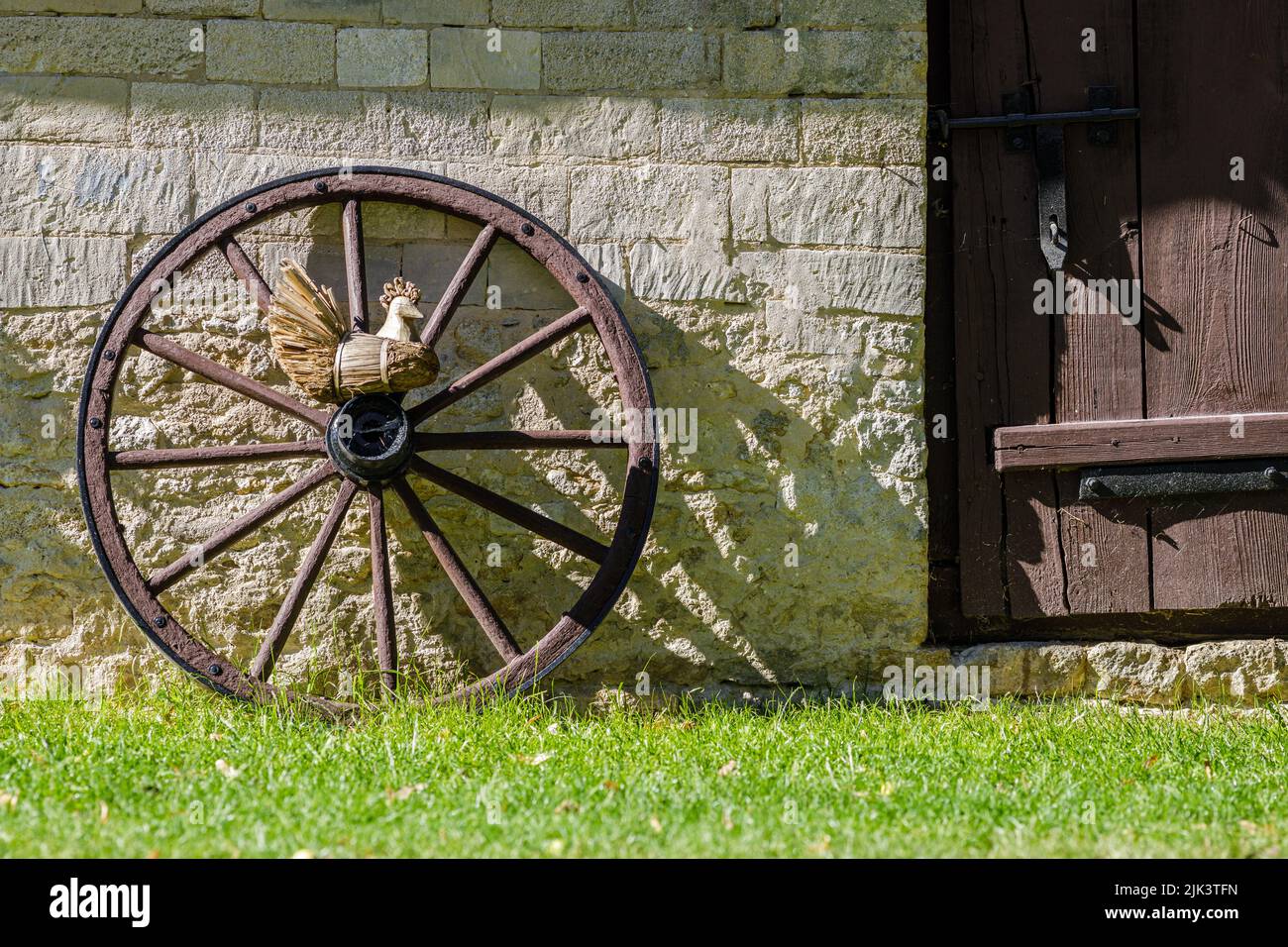Rural scene, wooden wheel from carriage against brick wall and wooden door Stock Photo