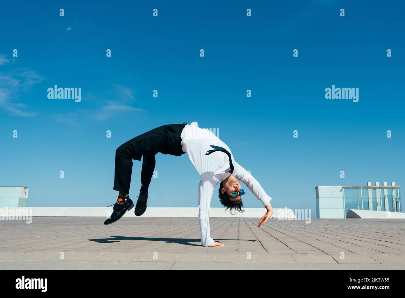 Happy and handsome adult businessman wearing elegant suit doing acrobatic trick moves in the city, alternative concept for business advertisement with Stock Photo
