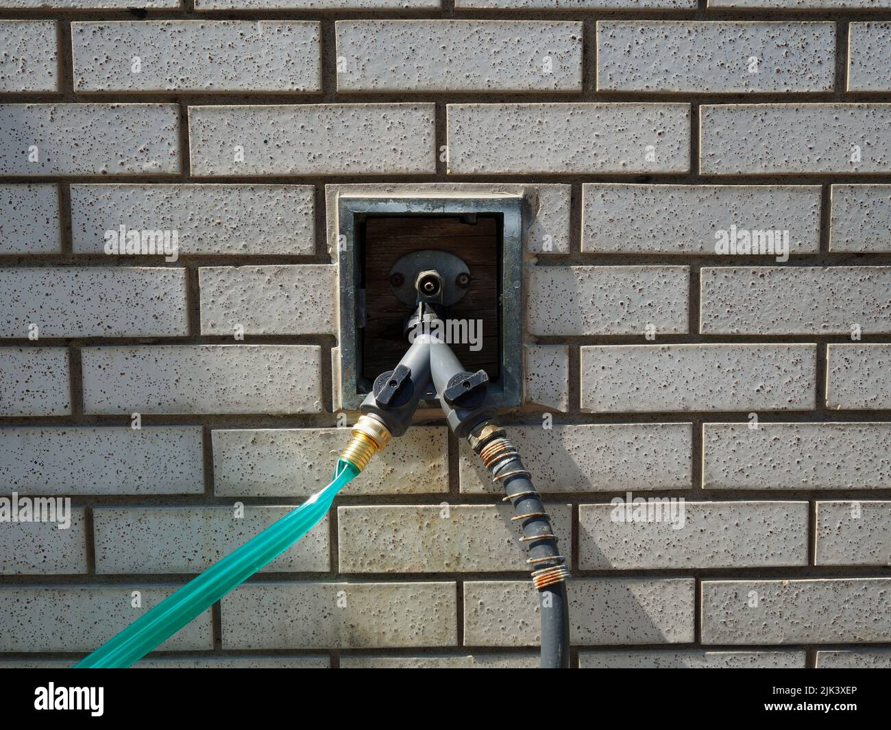 Detail of an outdoor tap built into a white brick wall with two hoses attached. Stock Photo