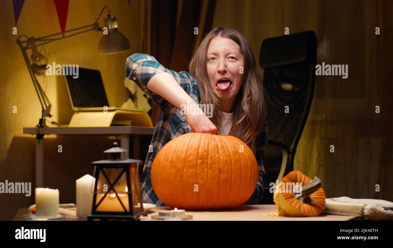 Preparing pumpkin for Halloween. Pulling out guts and seeds and being grossed out by it. Woman sitting and carving halloween Jack O Lantern pumpkin at Stock Photo