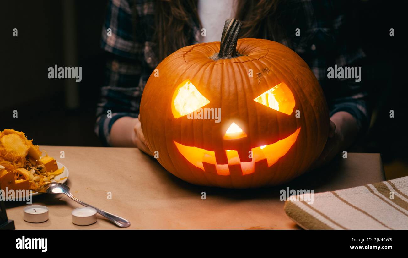 Illuminated pumpkin for Halloween. Woman sitting and showing out candle lit halloween Jack O Lantern pumpkin at home for her family. Stock Photo