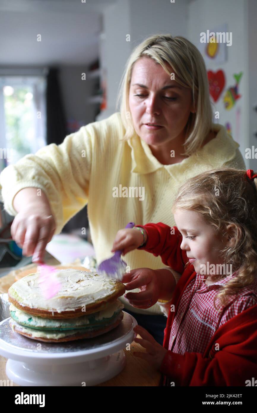 A mum and her young daughter in school uniform baking and decorating a