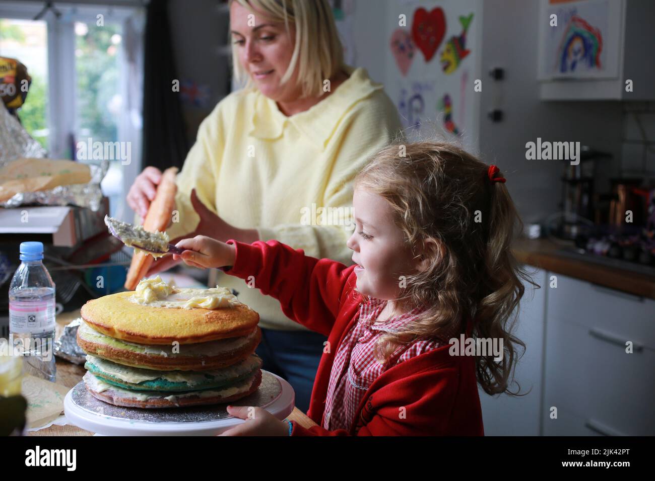 A mum and her young daughter in school uniform baking and decorating a cake, UK Stock Photo