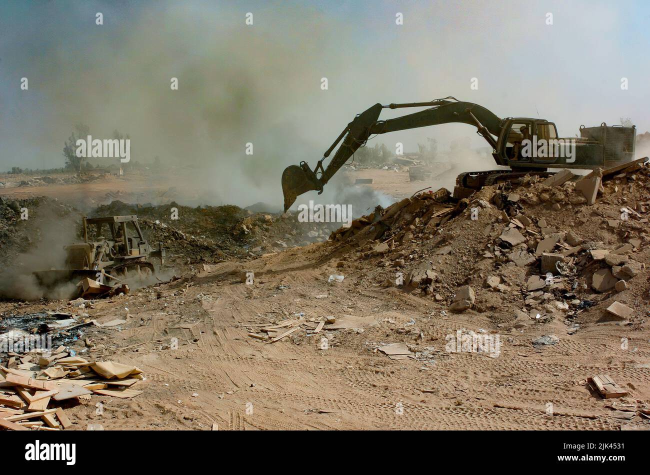 (LOGISTICS SUPPORT AREA ANACONDA, Balad, Iraq) - Soldiers from the 84th Combat Engineer Battalion use a bulldozer and excavator to manuever trash and other burnable items around in the burn pit at the landfill here. The bulldozer is primarily used to keep refuse constantly burning, and the excavator to push dirt over chutes to make the land useable in the future. Stock Photo