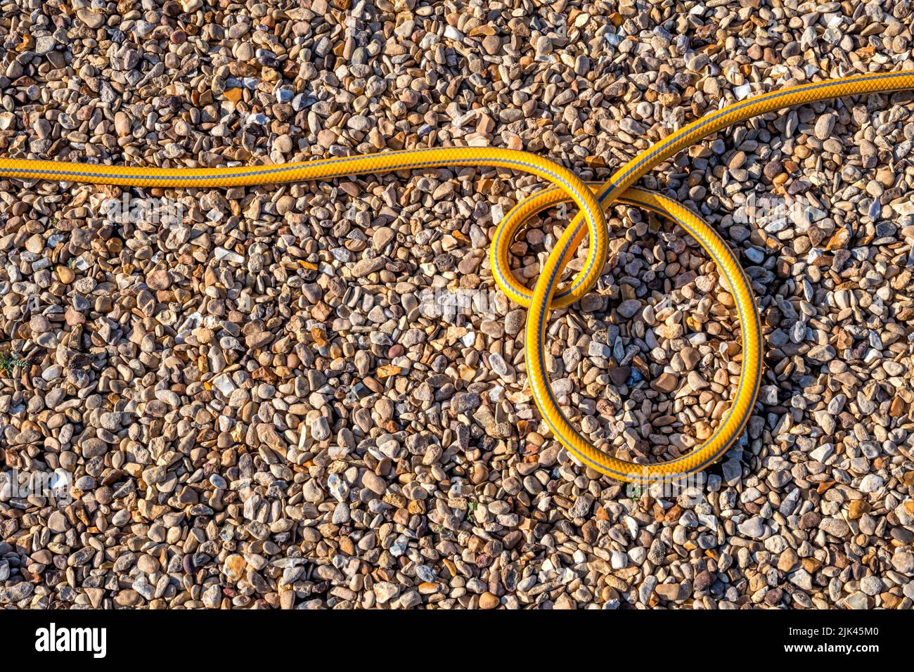 Coils of a garden hosepipe on a gravel drive. Stock Photo