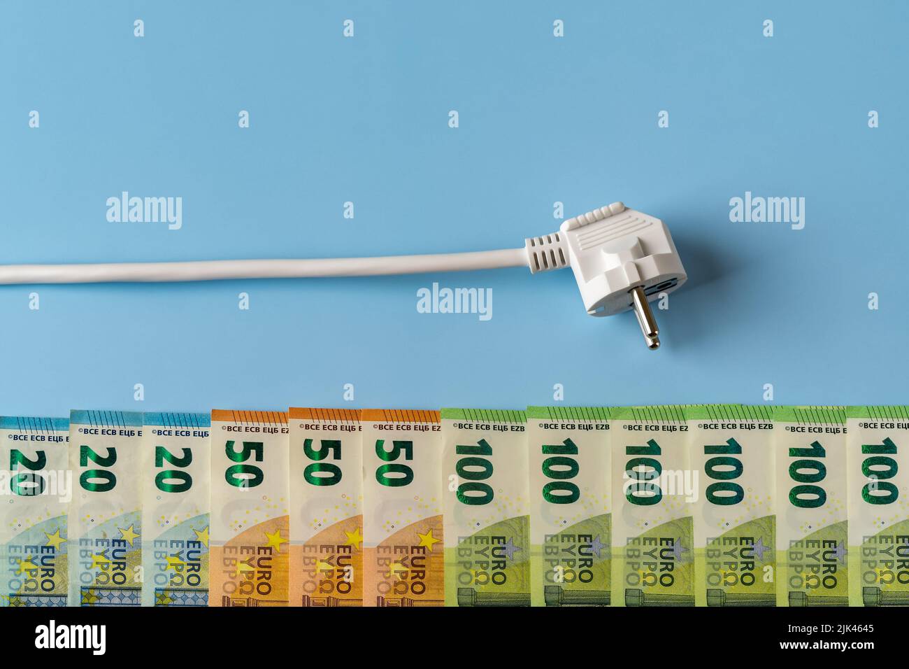 Power plug above row of euro money banknotes against blue background. Concept of rising energy bills and electricity price spike. High energy costs. Stock Photo