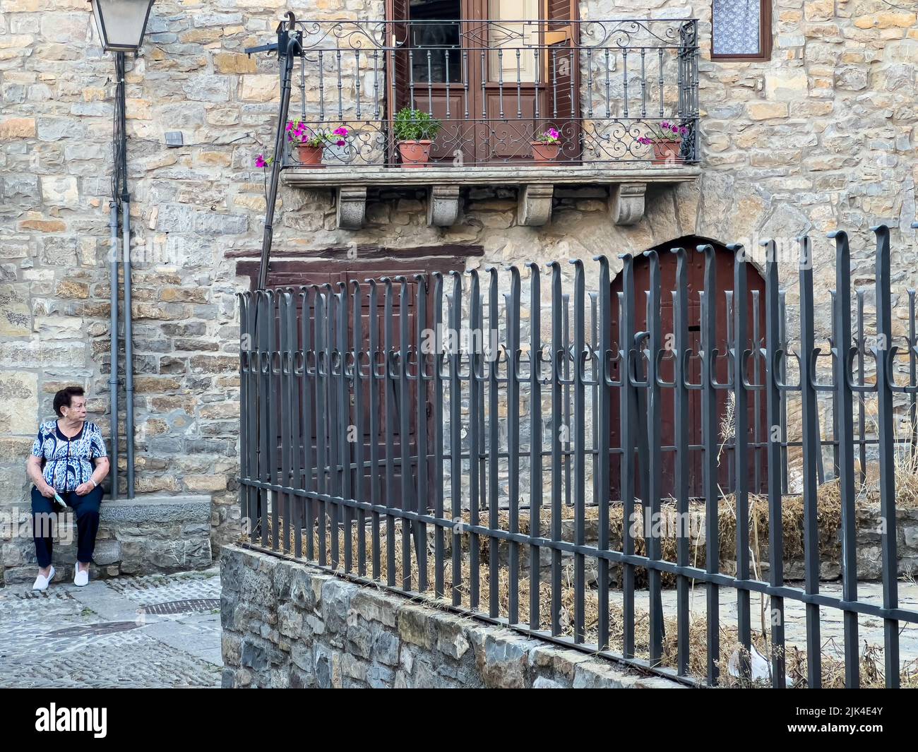 a lady sits against a stone wall in the town of Ainsa Spain Stock Photo