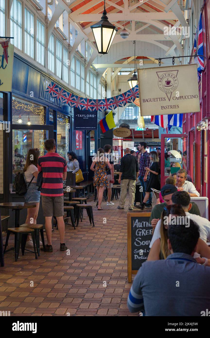 Interior of the Covered Market with people walking past shops and seated outside small restaurants, Oxford, UK Stock Photo