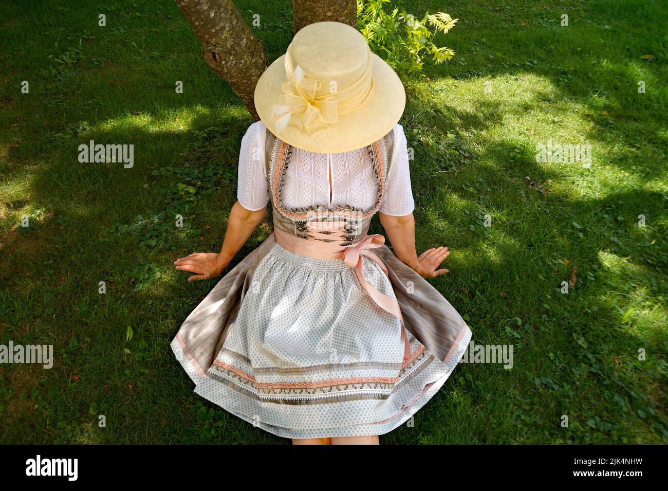a woman in a beautiful traditional Bavarian dirndl dress (or Tracht) resting on the green meadow on a sunny summer day (Munich, Bavaria, German Stock Photo