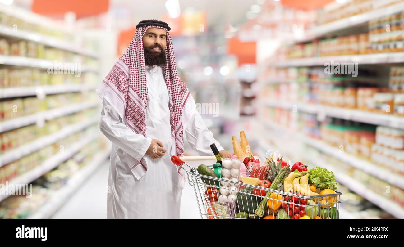 Saudi arab man with a shopping cart full of food products inside a supermarket Stock Photo