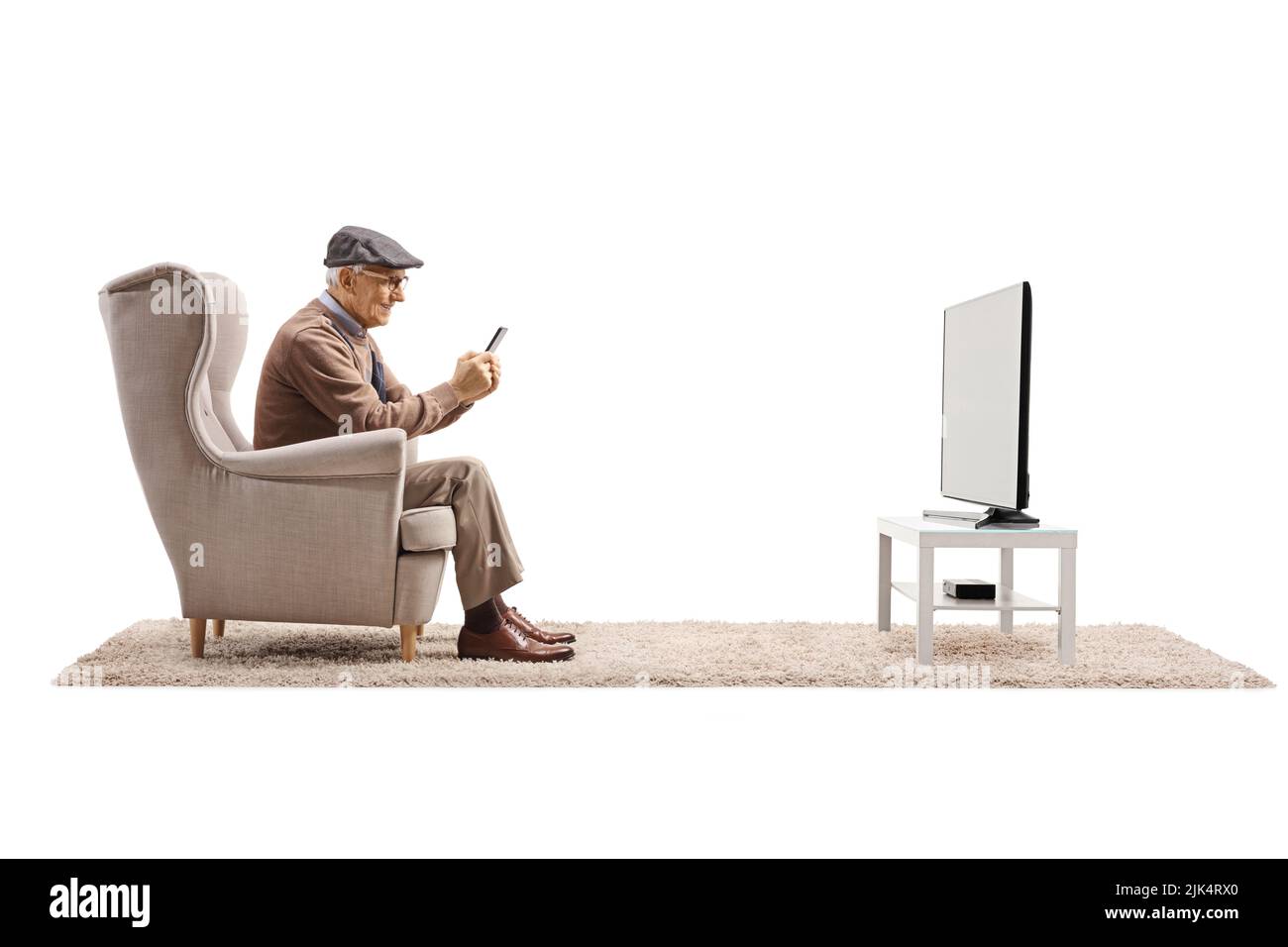 Elderly man in an armchair sitting in front of a TV and using a smartphone isolated on white background Stock Photo