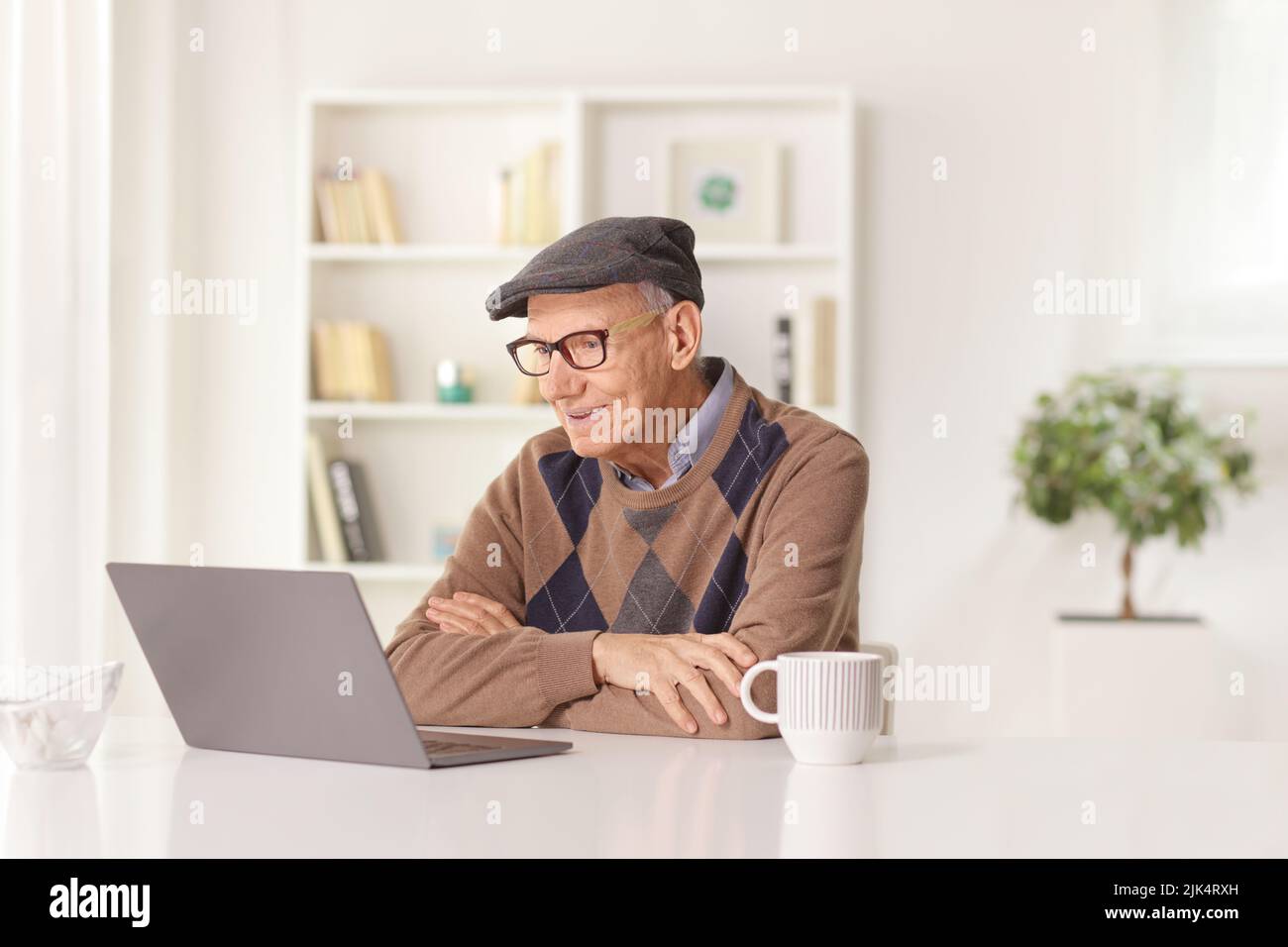 Happy elderly man sitting at a desk at home and looking at a laptop computer Stock Photo