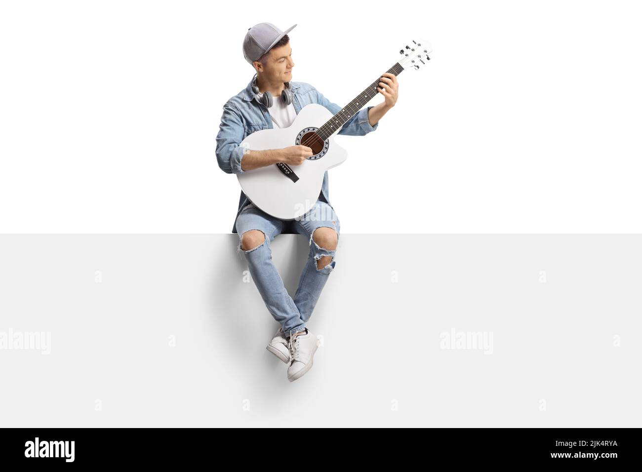 Guy sitting on a blank panel and playing an acoustic guitar isolated on ...