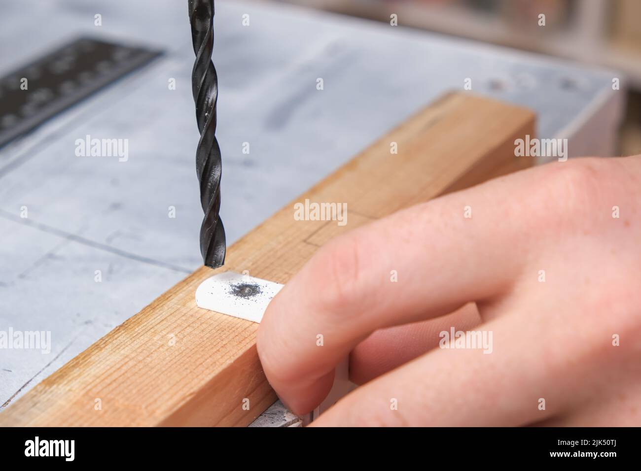 A man drills holes in an iron hook with a drill to hang a wooden screen