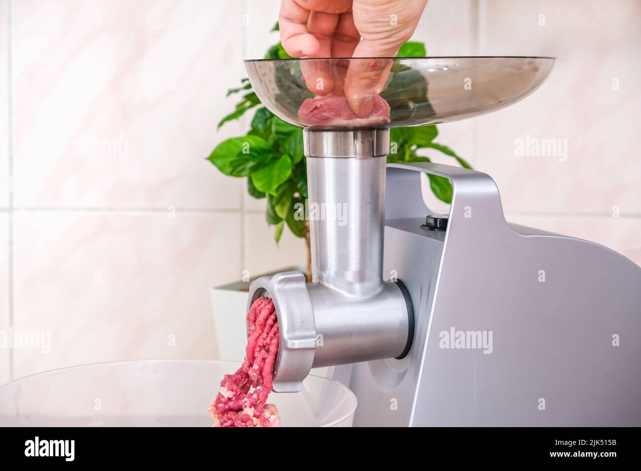 A man puts a piece of meat into an electric meat grinder. Preparation