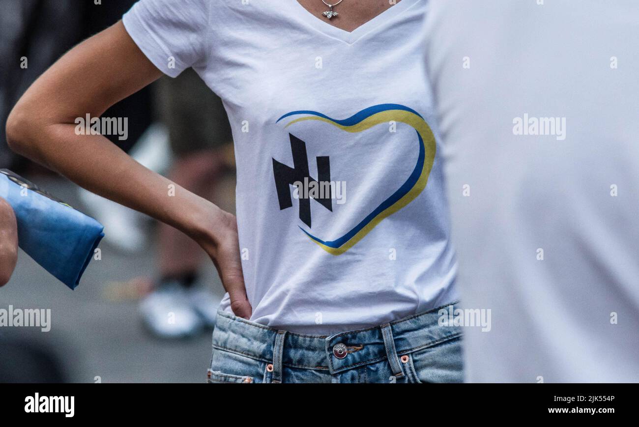 July 30, 2022, Munich, Bavaria, Germany: A woman in Munich, Germany wears a shirt with the highly controversial Wolfsangel which was also used by the Azov Battalion before it was dissolved. To date, there is no credible presence of neonazis or far-right influence on the Ukrainian demos and community organizing. After shocking video surfaced of a bound Ukrainian soldier being castrated by Russian invading forces, and a strike that killed at least 40 prisoners of war, Ukrainians protested against the atrocities being committed by Russian forces and demanded the allied countries do more to stop Stock Photo