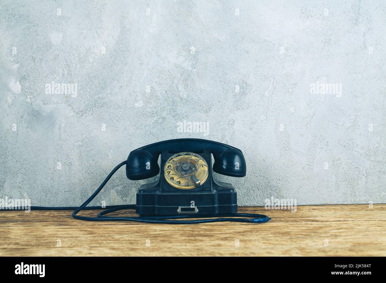 Retro black rotary telephone on wooden table in front gray concrete background Stock Photo