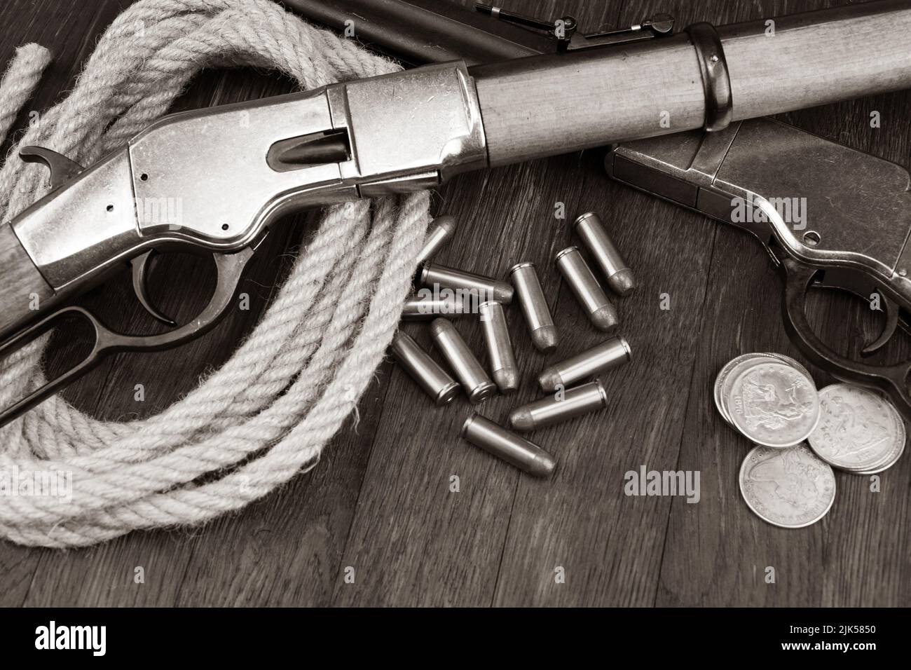 Old west guns - lever-action repeating rifles with ammunition and silver dollar coins on wooden table. Sepia tone. Stock Photo
