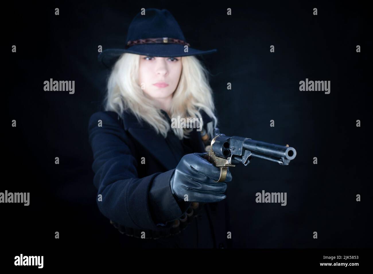 Old west blonde girl wearing black hat with revolver handgun on black background Stock Photo