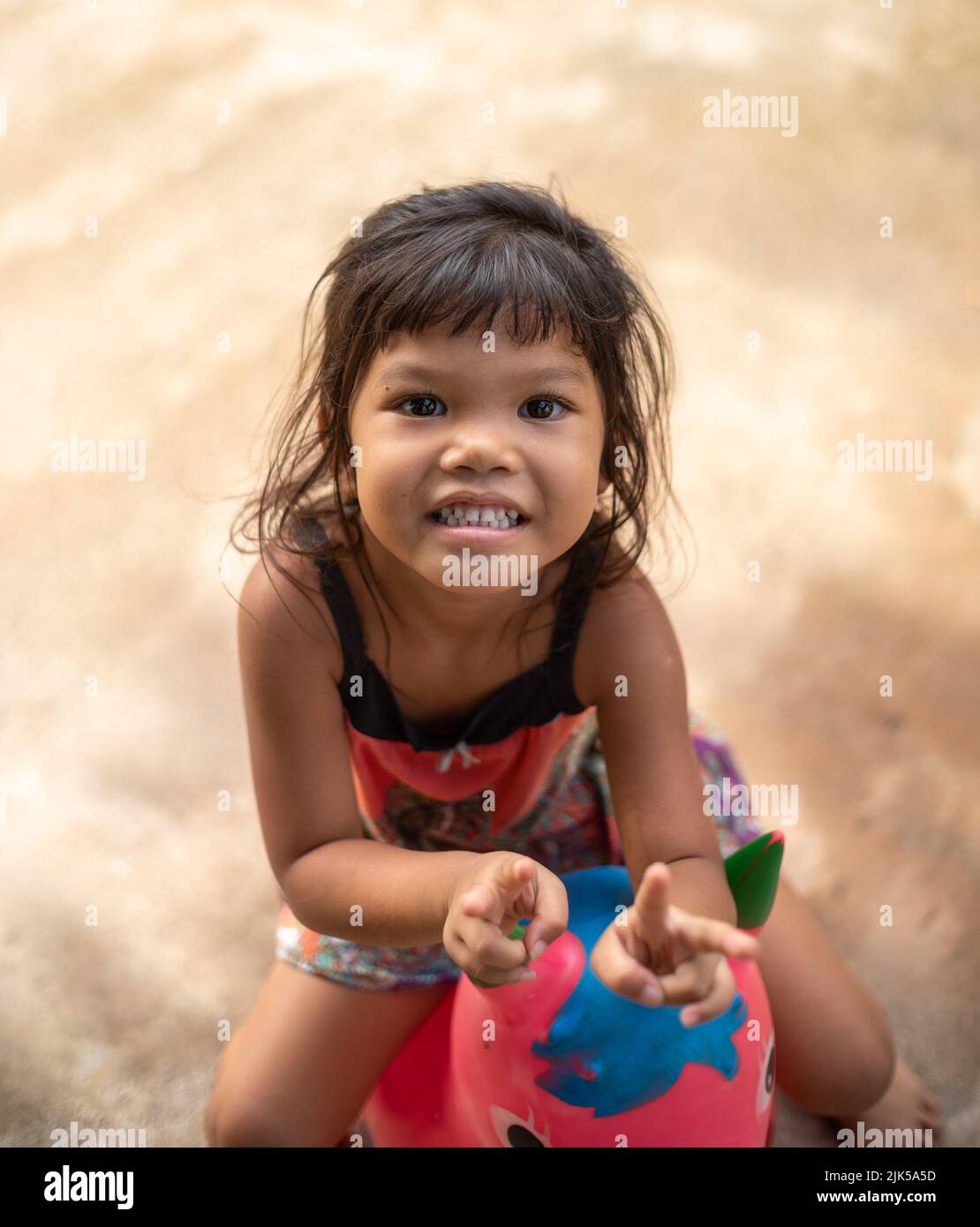 A young Thai girl smiles at the camera while sitting on a space hopper toy Stock Photo