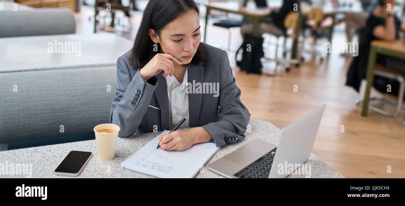 Young serious Asian business woman using laptop working in modern office. Stock Photo