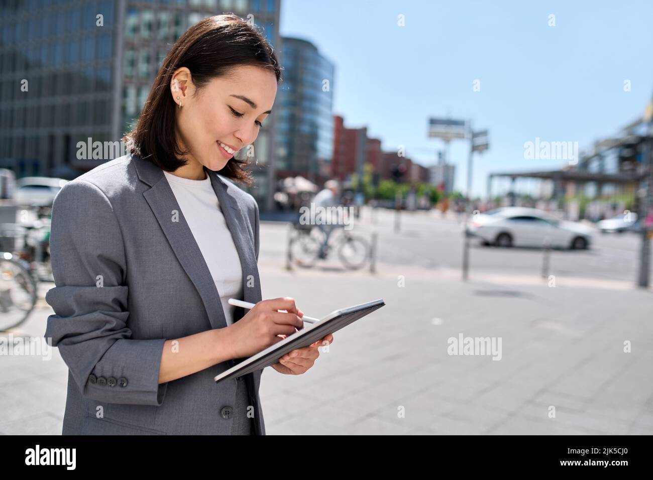 Young happy Asian business woman executive using digital tablet on city street. Stock Photo