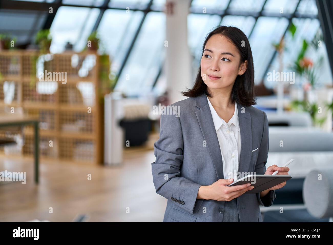 Young Asian business woman standing in office holding digital tablet. Stock Photo