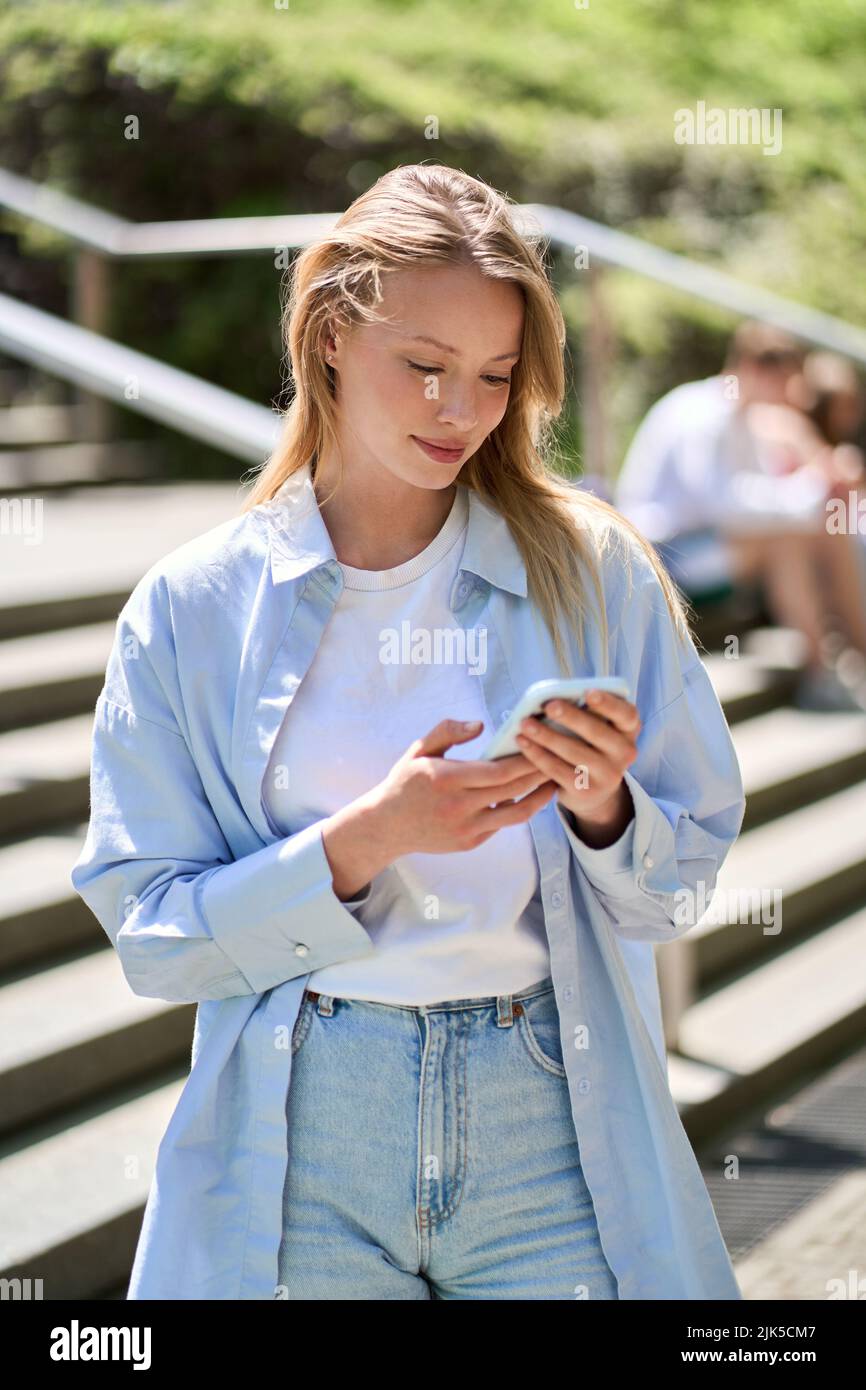 Young woman student using mobile apps on smartphone standing outdoors. Stock Photo