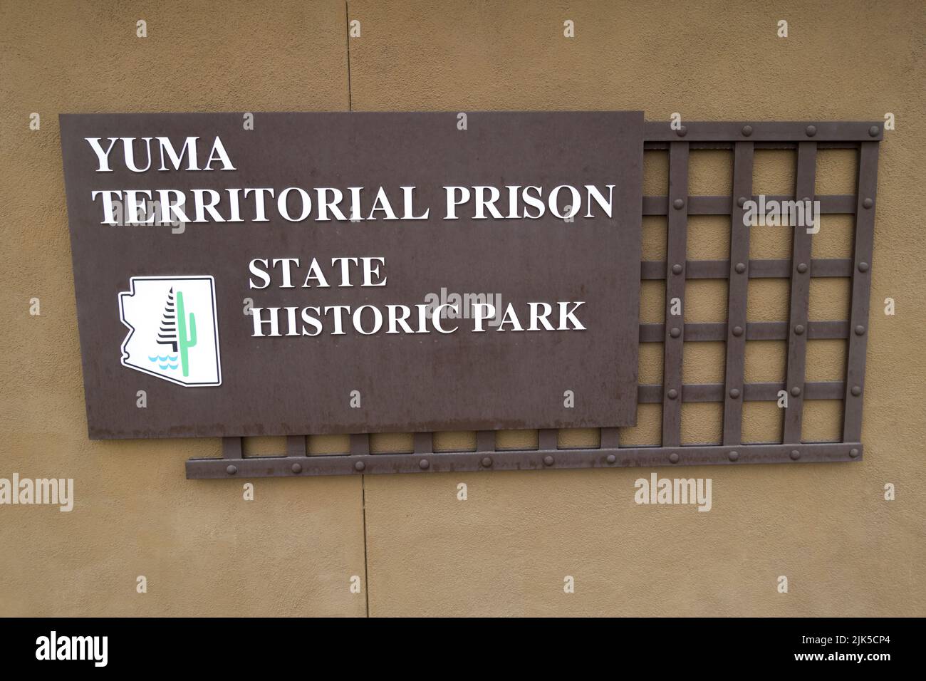 Information Table with Text against Brown Wall and Iron Bars at Entrance Gate to Famous Yuma Territorial Prison Arizona USA State Historic Park Stock Photo
