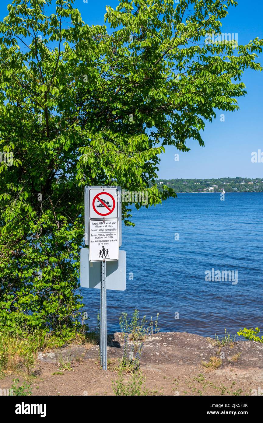 Bilingual no swimming sign by river. Stock Photo