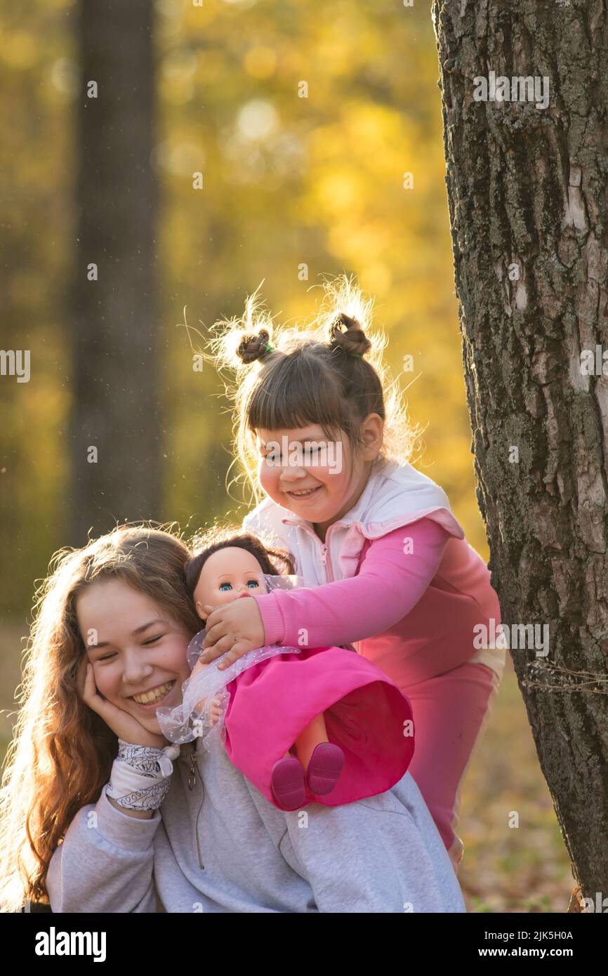 Two sisters sitting on the ground in autumn park by the tree - a little ...