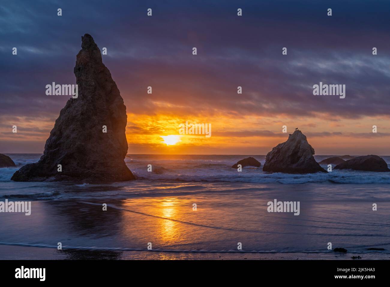 Sun and sky reflected on Bandon Beach at sunset with sea stacks in silhouette on the Pacific Coast in Bandon, Oregon. Stock Photo