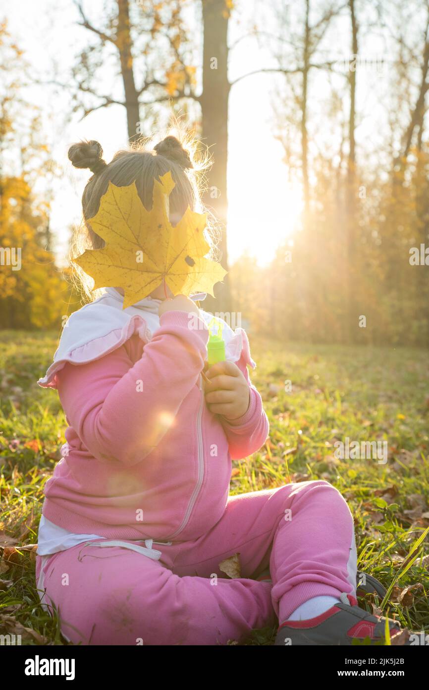 A little girl in pink costume sitting on the ground in autumn park and ...